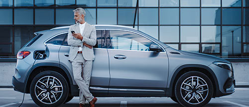 Mann lehnt an ladendem E-Auto